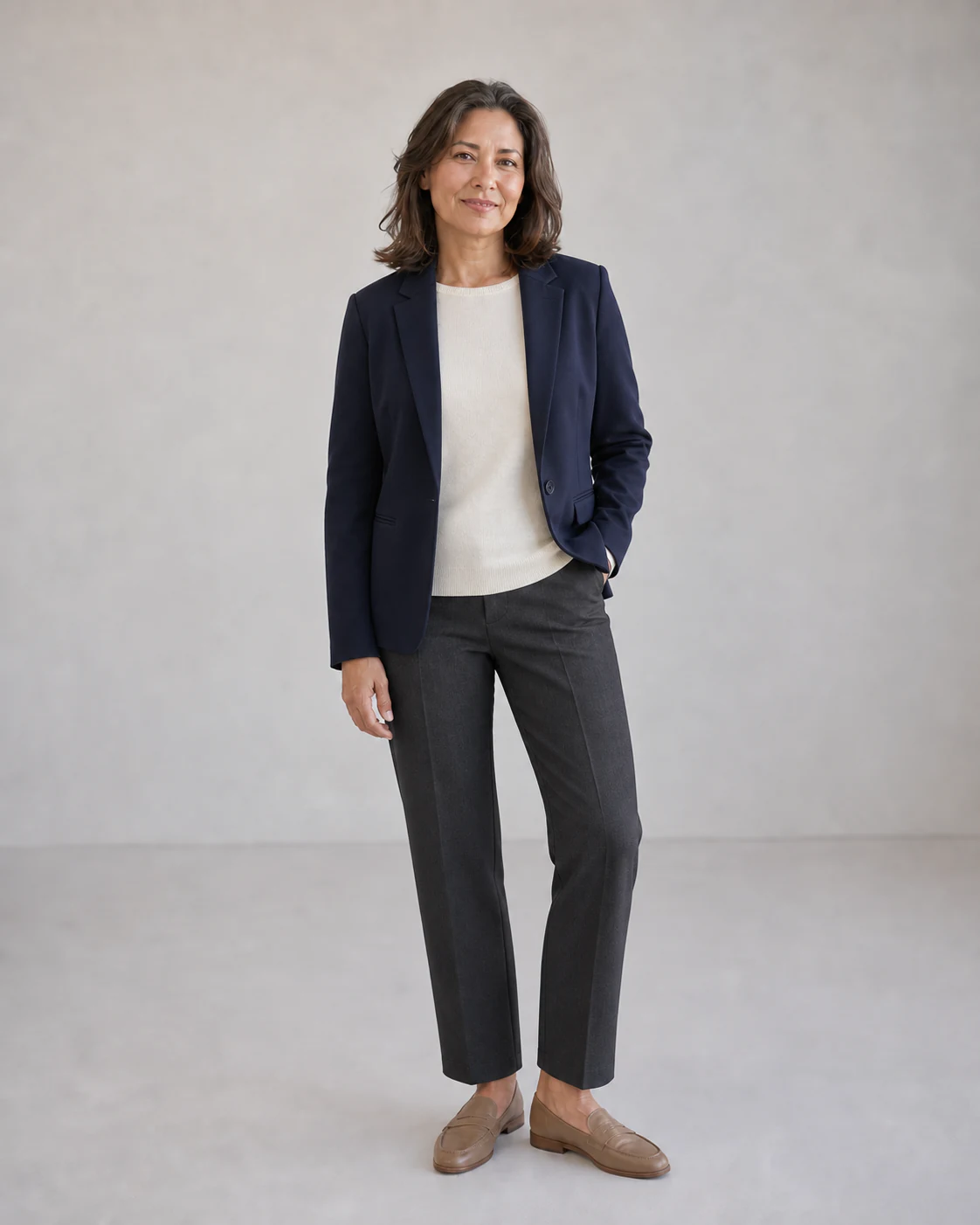 The same fictional 48-year-old model in an easy soft navy blazer, ivory knit, charcoal trousers, and taupe loafers